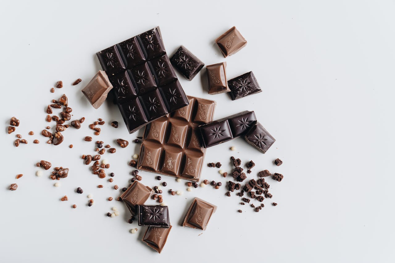 Artistic arrangement of dark and milk chocolate bars with crumbs on a white surface.