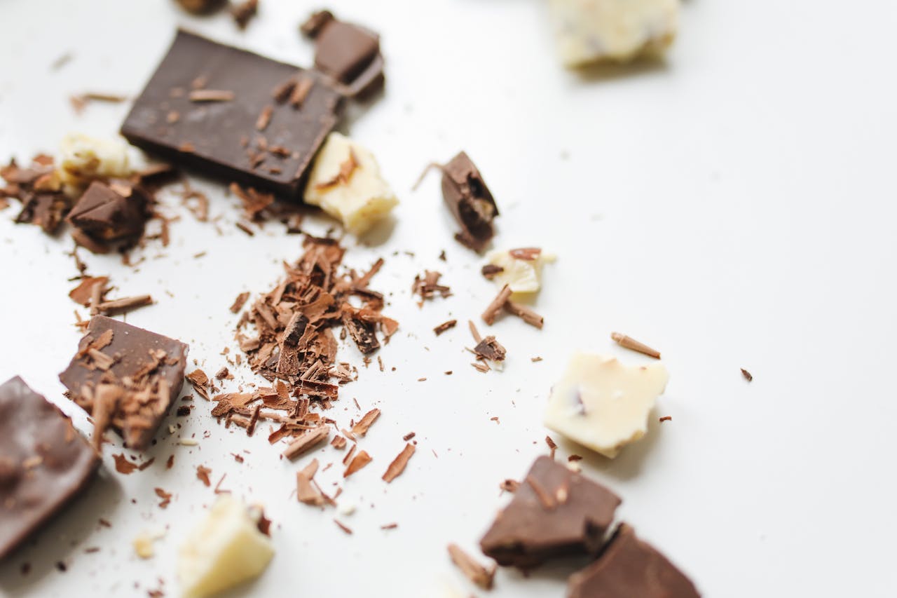 Scattered chocolate chunks and shavings on a white background, showcasing dessert ingredients.