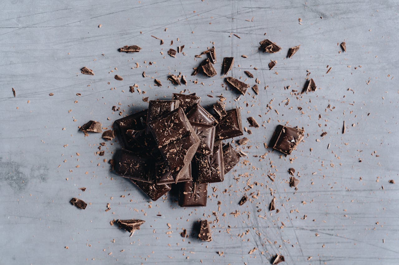 Top-down view of broken dark chocolate bars with shavings on a gray background, ideal for food photography.